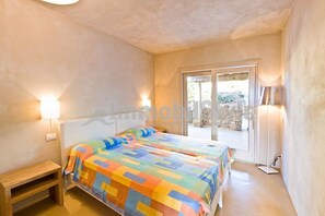 A bedroom with a bed, bedside table, and a view through a glass door to an outdoor area. - Exclusive villa with private pool (Santa Reparata)