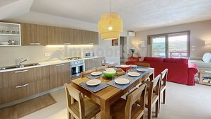 A modern kitchen with wooden cabinets, a dining table set for four, and a red sofa in the living area. - Exclusive villa with private pool (Santa Reparata)