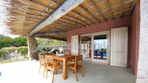 A covered patio with a wooden table and chairs, a concrete floor, and a door leading to an interior space. - Exclusive villa with private pool (Santa Reparata)