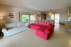 Amplia sala de estar con un sofá blanco y un sofá rojo, zona de comedor con mesa y sillas, y cocina con microondas y armarios.