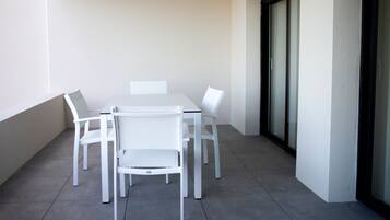 Une table blanche et quatre chaises sur un balcon doté d’un sol carrelé et d’une porte vitrée.