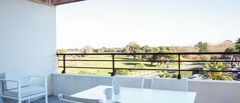 A balcony with a white table and chairs, a white sofa, and a view of a golf course and parking area.