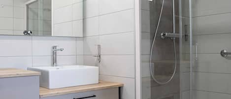 Un baño moderno con cabina de ducha acristalada, un lavabo blanco y un espejo encima.