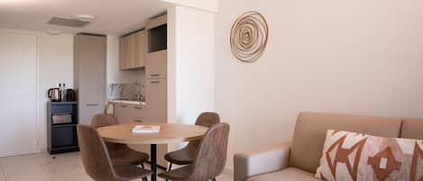 A modern living room with a beige sofa, a round dining table with four chairs, and a kitchen area in the background.