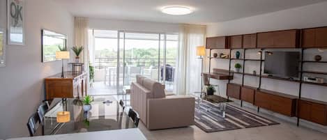 A modern living room with a sofa, dining table, and kitchen area with cabinets and a TV.