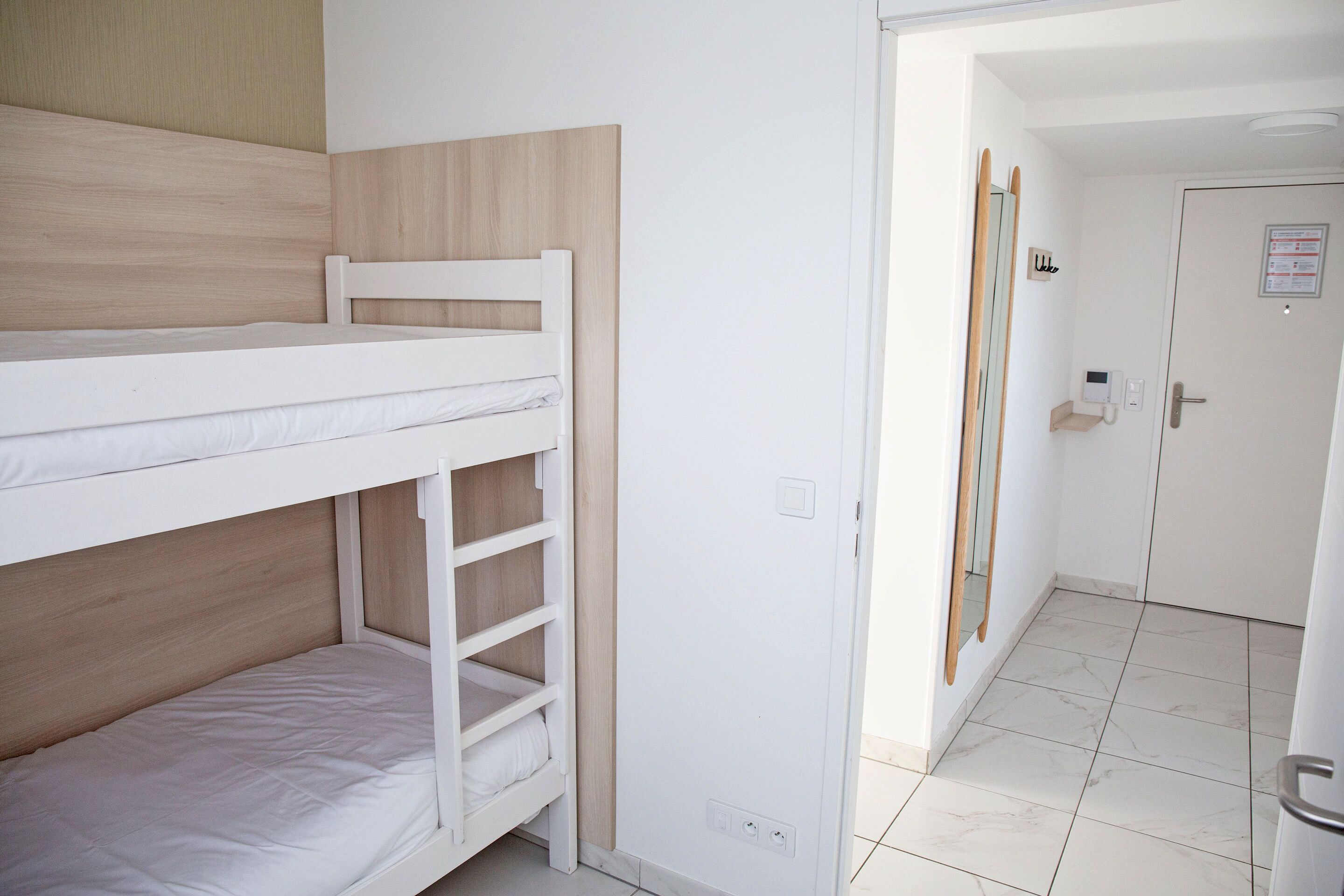 A bunk bed room with a wooden headboard, a white door with a sign, and a tiled floor.