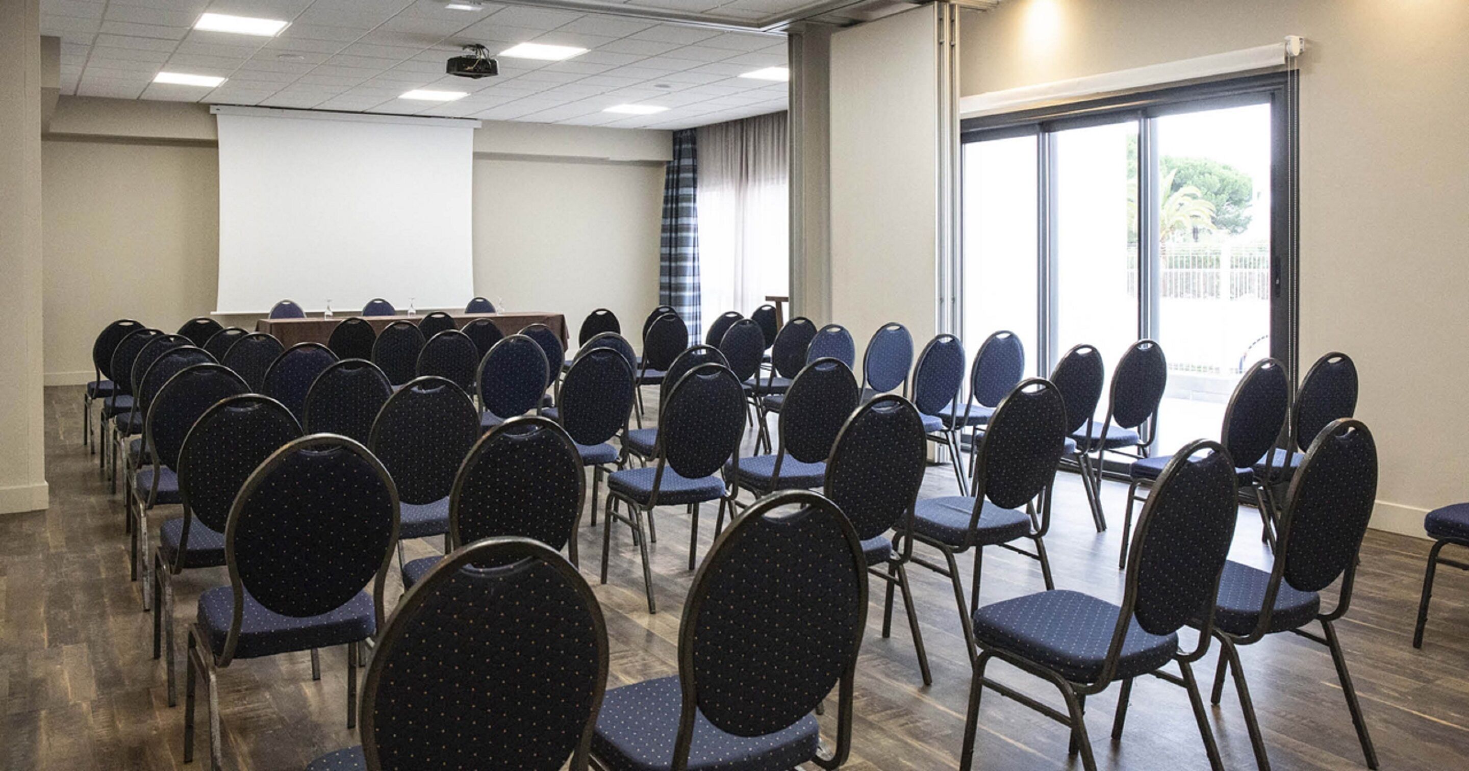 A conference room with rows of chairs, a projector screen, and a large window.