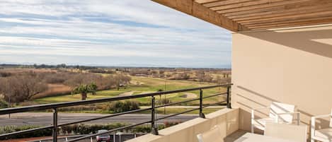 Un balcón con vista a un campo de golf, una mesa y sillas.