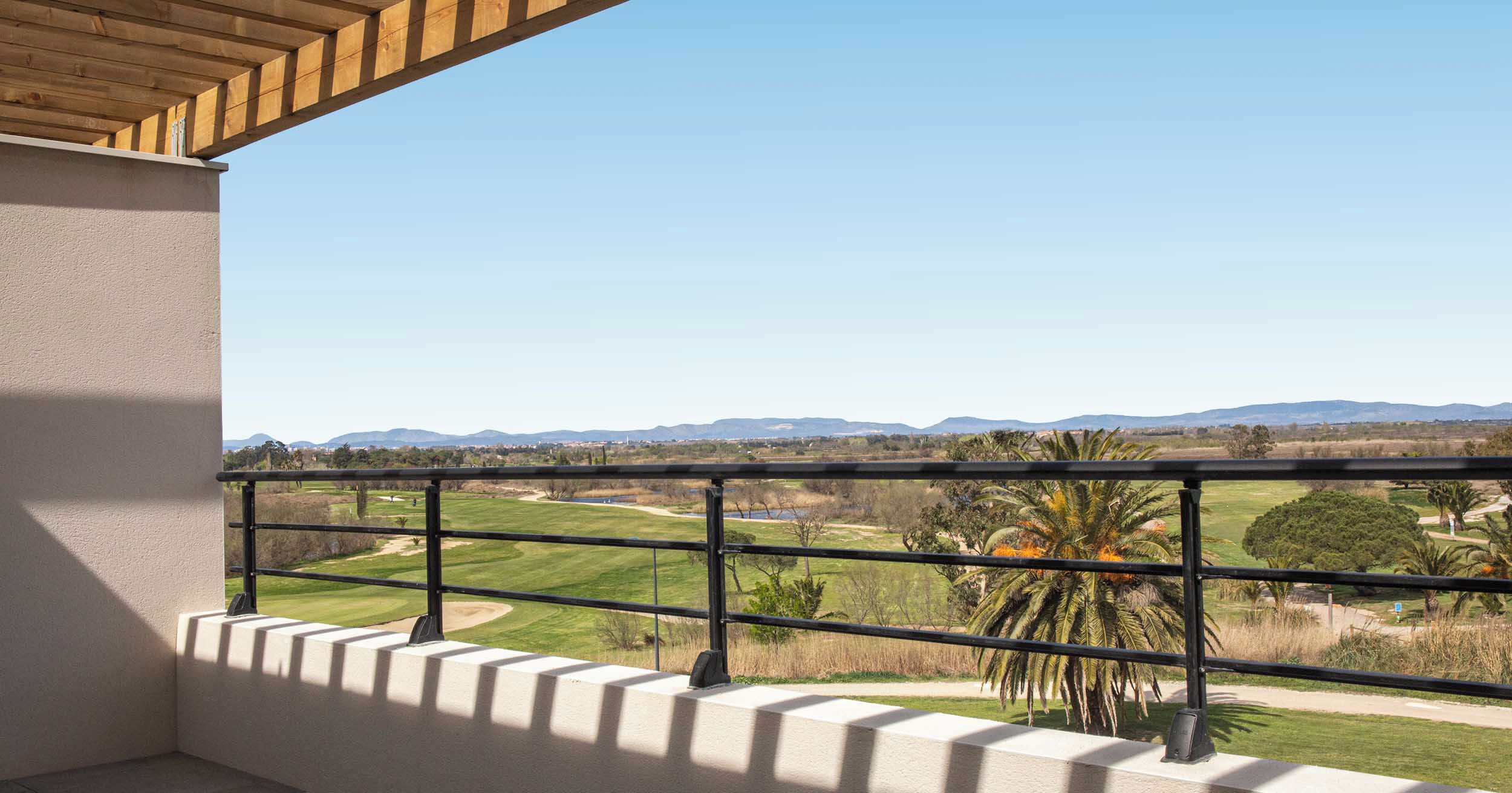 A balcony with a view of a golf course and distant mountains.