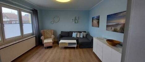 Una sala de estar con sofá, sillón, mesa de centro y aparador con un cuenco.