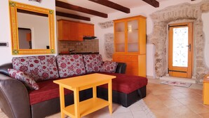 A cozy living room with a sofa, a small table, a TV, and a kitchen area with cabinets and a stone wall. - Vacation apartment with private swimming pool (Kukljica)