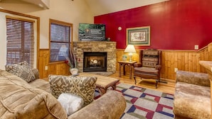 Un salon chaleureux avec une cheminée en pierre, des meubles en bois et un mur d’accent de couleur rouge.