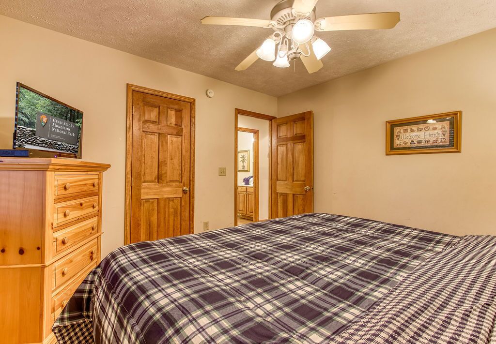 A bedroom with a plaid bedspread, wooden dresser, and a ceiling fan.
