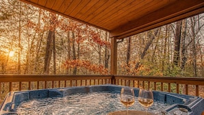 Un bain à remous avec deux verres de vin, sur une terrasse en bois offrant une vue sur la forêt.