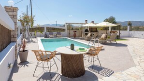 A rooftop pool area with a table and chairs, a pergola with an umbrella, and a stone wall.