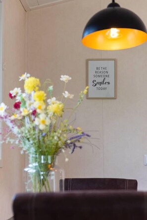A dining area with a table, chairs, a vase of flowers, a wall-mounted light fixture, and a framed inspirational quote. - Enjoyin Luxury Chalet With Swimming Pool (Schoonebeek)