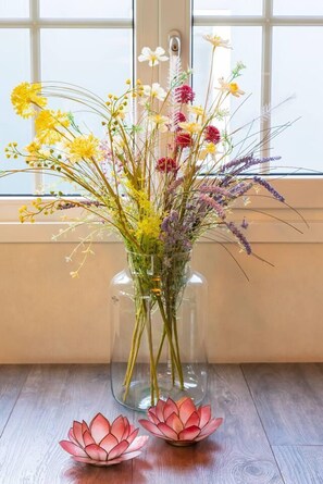 Eine klare Glasvase mit verschiedenen Blumen auf einem Holztisch neben einem Fenster.