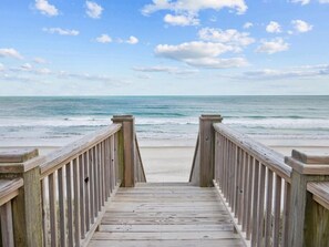 A wooden boardwalk leading to a beach with a clear view of the ocean.