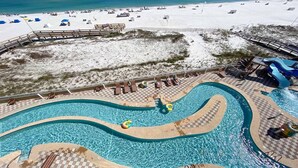 A pool area with a checkered deck, a water slide, and a beach in the background. - New to the Rental Market, Lazy River and Slide, Beachfront!! (Orange Beach)