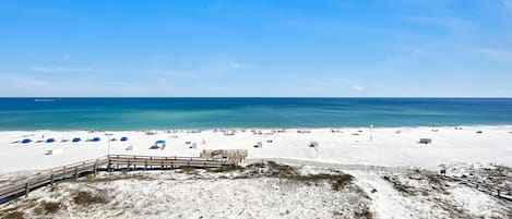 A beach with a wooden boardwalk leading to a sandy area with beach umbrellas and a lifeguard tower.