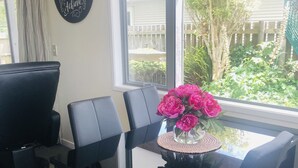 Een eetgedeelte met een glazen tafel, omringd door zwarte stoelen, een zwart kunstwerk met motiverende tekst, en uitzicht op een tuin door een groot raam.