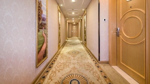 A hallway with a patterned carpet, a large framed painting on the left, and a wooden door with a number plaque on the right. - Vienna 3 Best Hotel (Guangzhou)