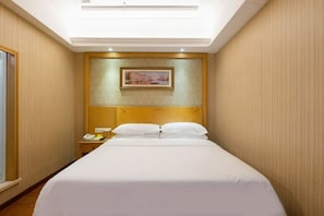 Una habitación de hotel con una cama grande, una mesita de noche con un teléfono y un cuadro en la pared.