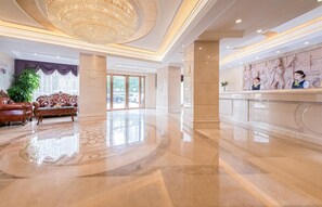 A hotel lobby with a reception desk, a plush sofa, and a large chandelier.