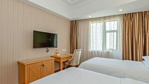Quarto de hotel com duas camas, televisão na parede, escrivaninha de madeira e uma cadeira.
