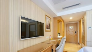 A hotel room with a large flat-screen TV mounted on the wall, a wooden desk with a chair, a bed, and a door leading to another room. - Vienna 3 Best Hotel (Guangzhou)