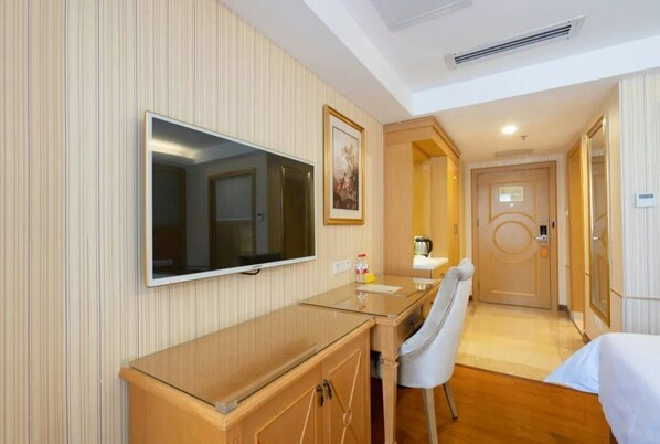 Habitación de hotel con una tele de pantalla plana grande montada en la pared, un escritorio de madera con una silla, una cama y una puerta que da a otra habitación.