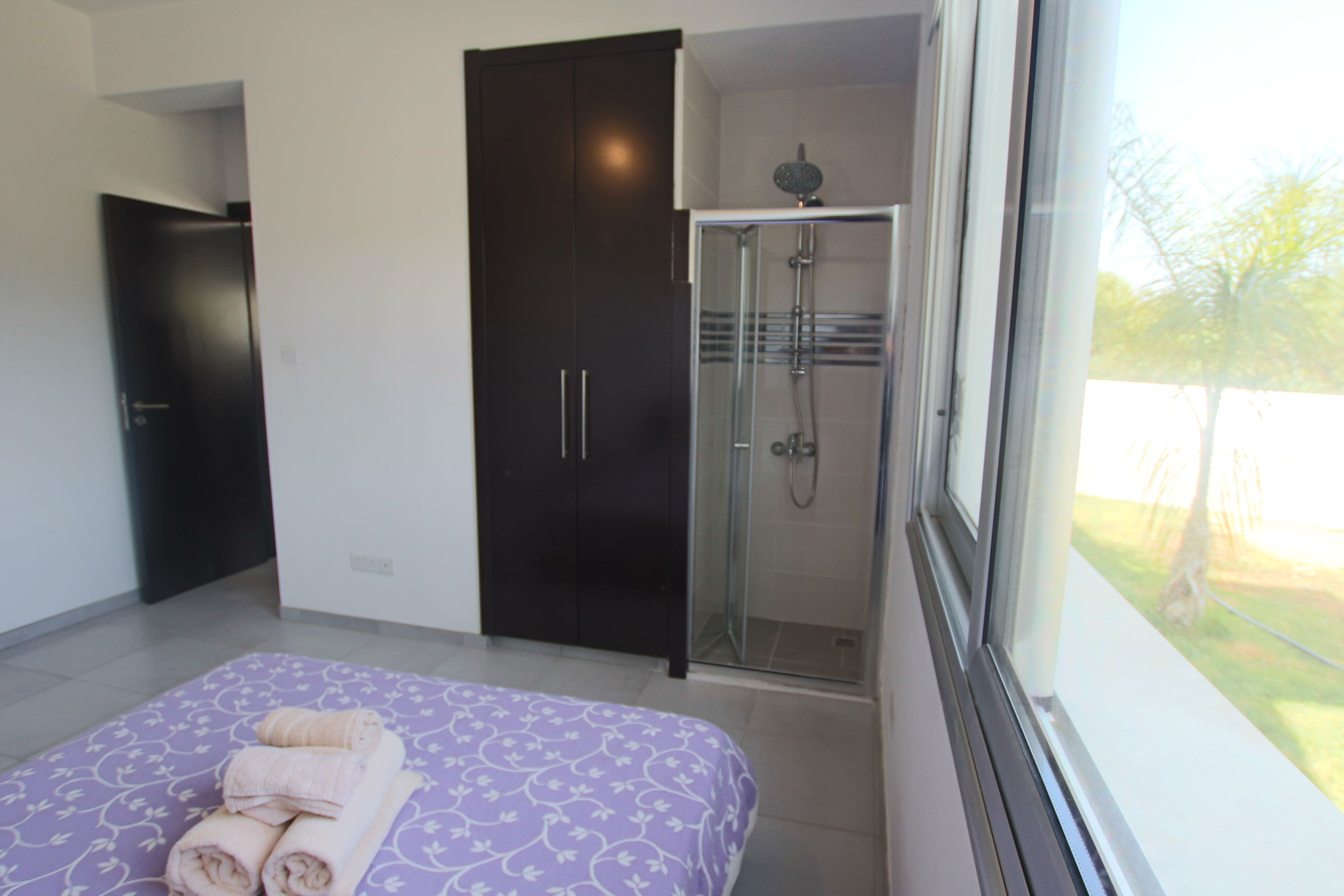 A bedroom with a bed, a walk-in closet, a shower, and a window with a view of the outdoors.