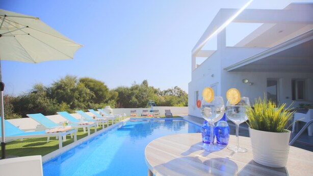 Un espace aménagé au bord de la piscine, avec des chaises longues, une table sur laquelle sont disposées des boissons et une plante.