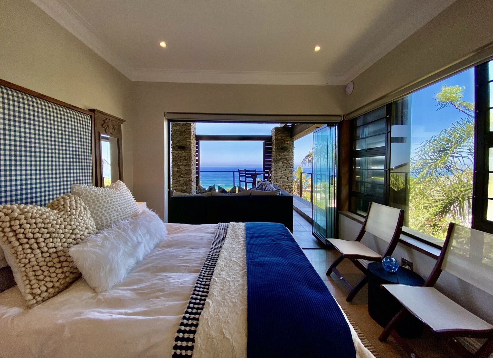 A bedroom with a large bed, a view of the ocean, and a balcony with a chair.