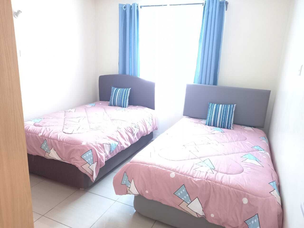 Two single beds with matching headboards and footboards, pink bedding with geometric patterns, and blue curtains on a window.