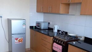 A compact kitchen with a refrigerator, microwave, stove, and a gas cylinder. - Lilly's Furnished Apartments (Nakuru)