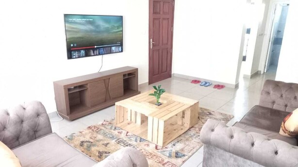 A living room with a television, a wooden coffee table, and two grey sofas. - Lilly's Furnished Apartments (Nakuru)