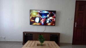 A living room with a television mounted on the wall, a wooden coffee table with a plant, and a patterned rug on the floor. - Lilly's Furnished Apartments (Nakuru)