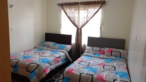 A room with two beds, each with a patterned bedspread and a headboard. There is a window with a sheer curtain and a visible light fixture on the ceiling. - Lilly's Furnished Apartments (Nakuru)