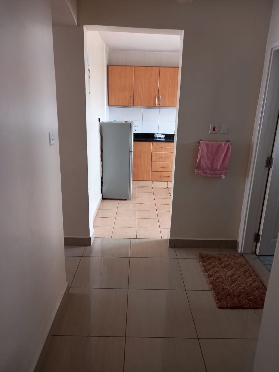 A hallway leading to a kitchen with cabinets, a refrigerator, and a tiled floor.