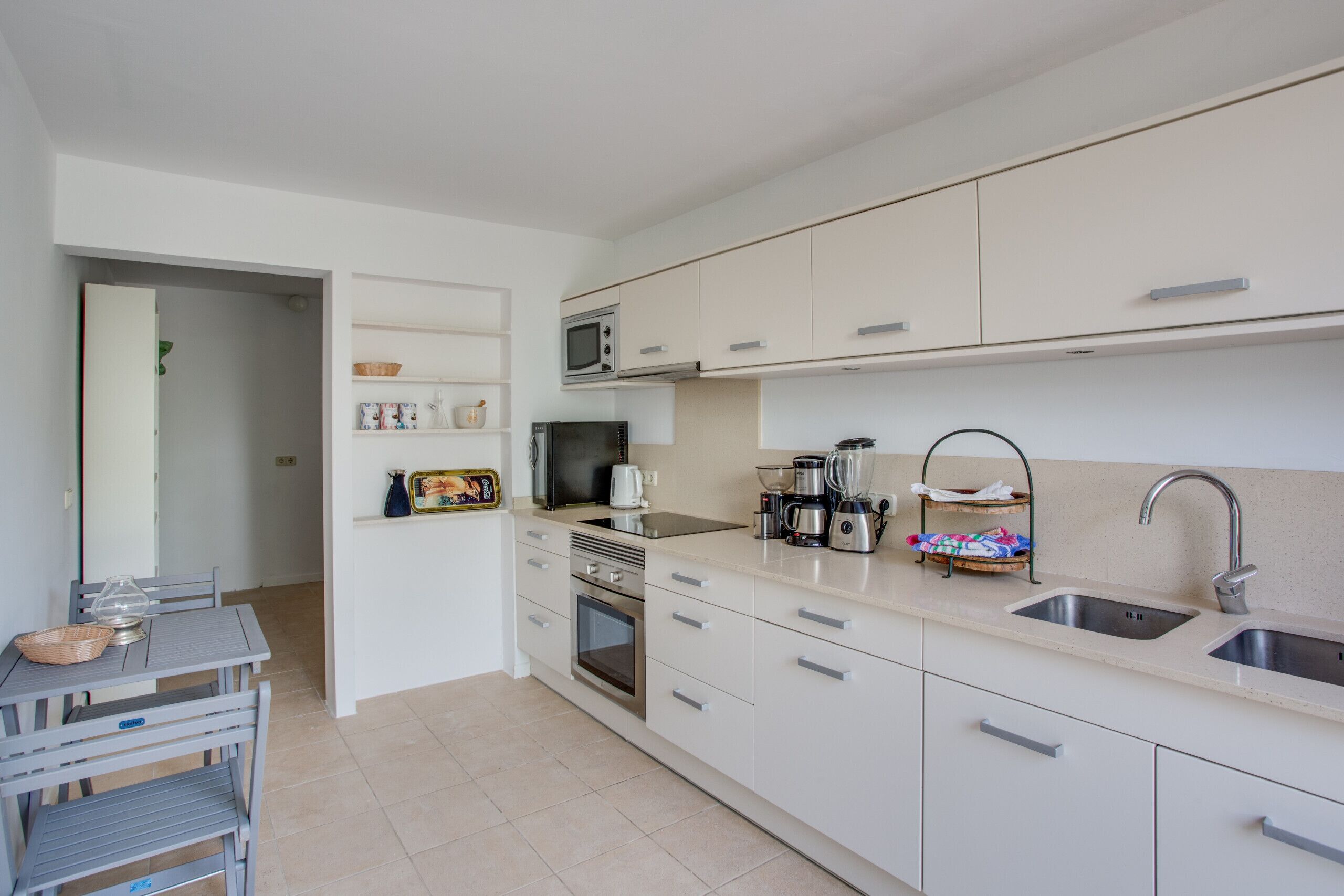 A modern kitchen with white cabinets, a built-in oven, a microwave, and a coffee maker.