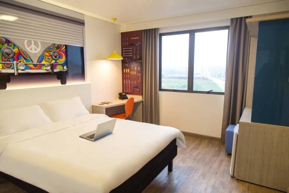 Habitación de hotel con cama, escritorio, silla, ordenador portátil, ventana con vistas y un diseño de símbolo de paz en la pared.