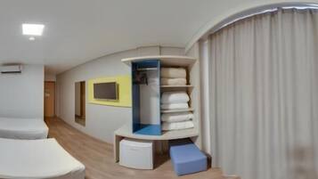 A modern hotel room with a curved layout, a built-in wardrobe, a seating area, and a small desk.