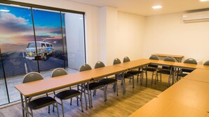Un salón de conferencias con una larga mesa y sillas, ventanas amplias con vista a una camioneta y un equipo de aire acondicionado en la pared.