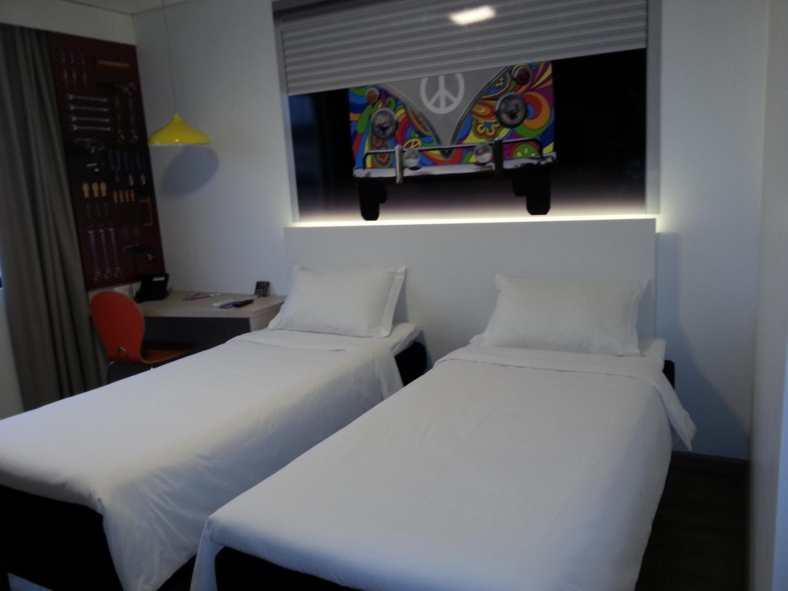 Een hotelkamer met twee eenpersoonsbedden, een bureau met stoel, een aan de muur bevestigde televisie en een lamp.
