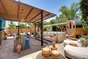 A covered outdoor seating area with a wooden pergola, a hot tub, and a wooden barrel structure.