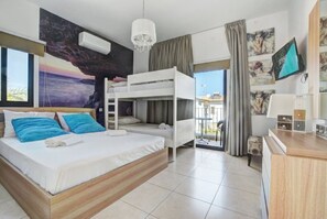 Ein Hotelzimmer mit einem Etagenbett, einem Schreibtisch, einem Fernseher und einem großen Fenster mit Meerblick.