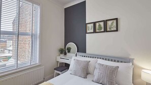 Un dormitorio con cama, mesita de noche, cómoda y ventana con persianas.
