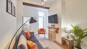 Una sala de estar moderna con un sofá gris, cojines naranjas, un aparador de madera, un televisor y una planta en maceta.