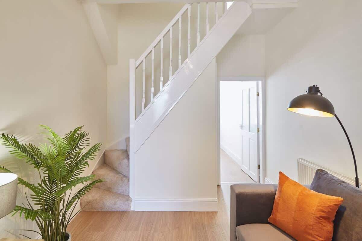 A staircase with white railings, a grey sofa with an orange pillow, and a floor lamp.